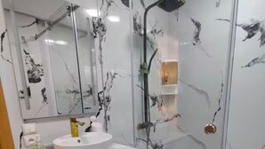 A modern bathroom with a glass-enclosed shower, a white sink, and marble-patterned walls.