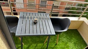 A balcony with a small table and two chairs, a metal railing, and a view of a building in the background.