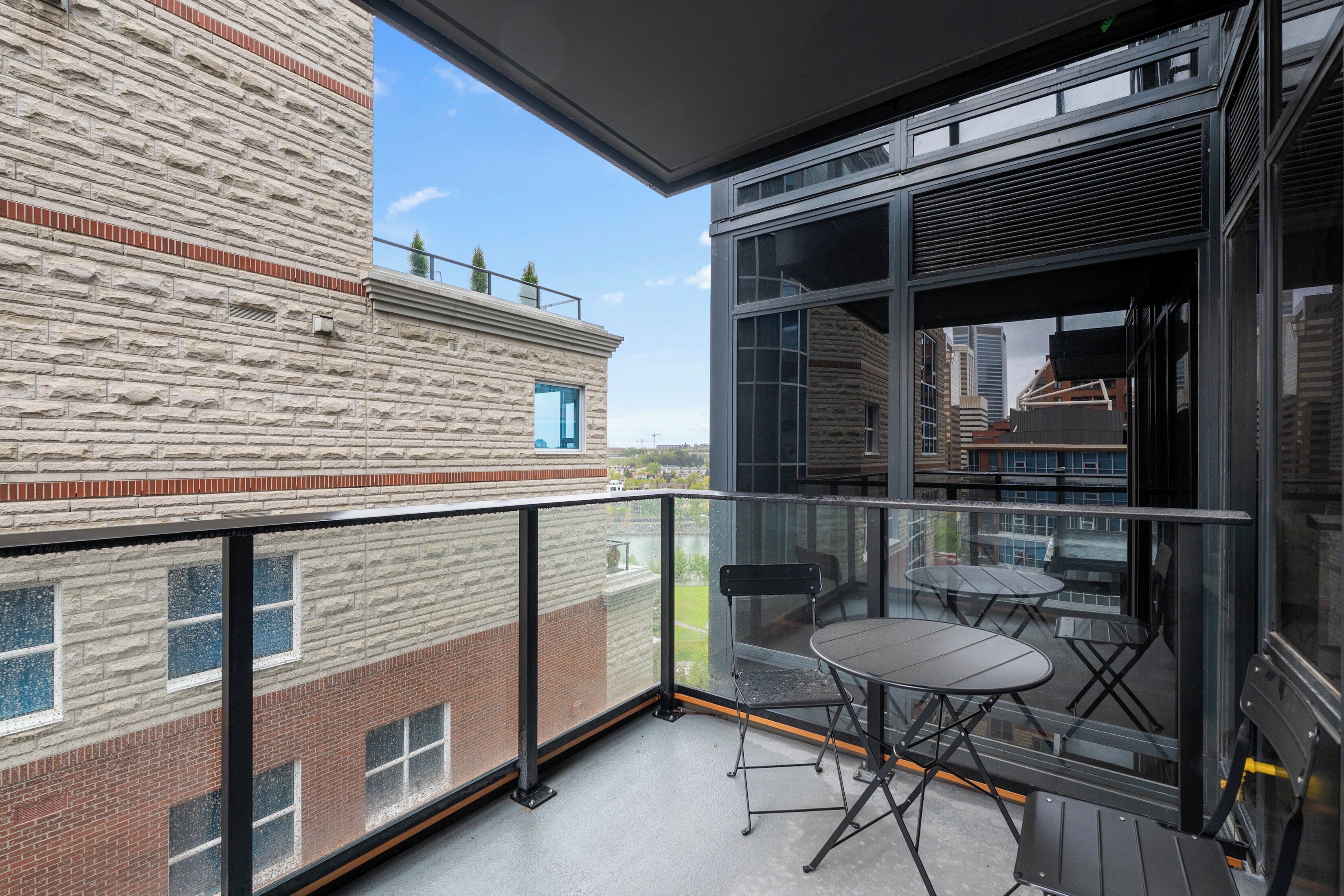 A balcony with a glass railing, two foldable chairs, and a table.