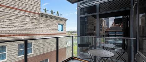 A balcony with a glass railing, two foldable chairs, and a table.