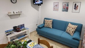 Una sala de estar con un sofá azul, un televisor montado en la pared y un pequeño estante con adornos.