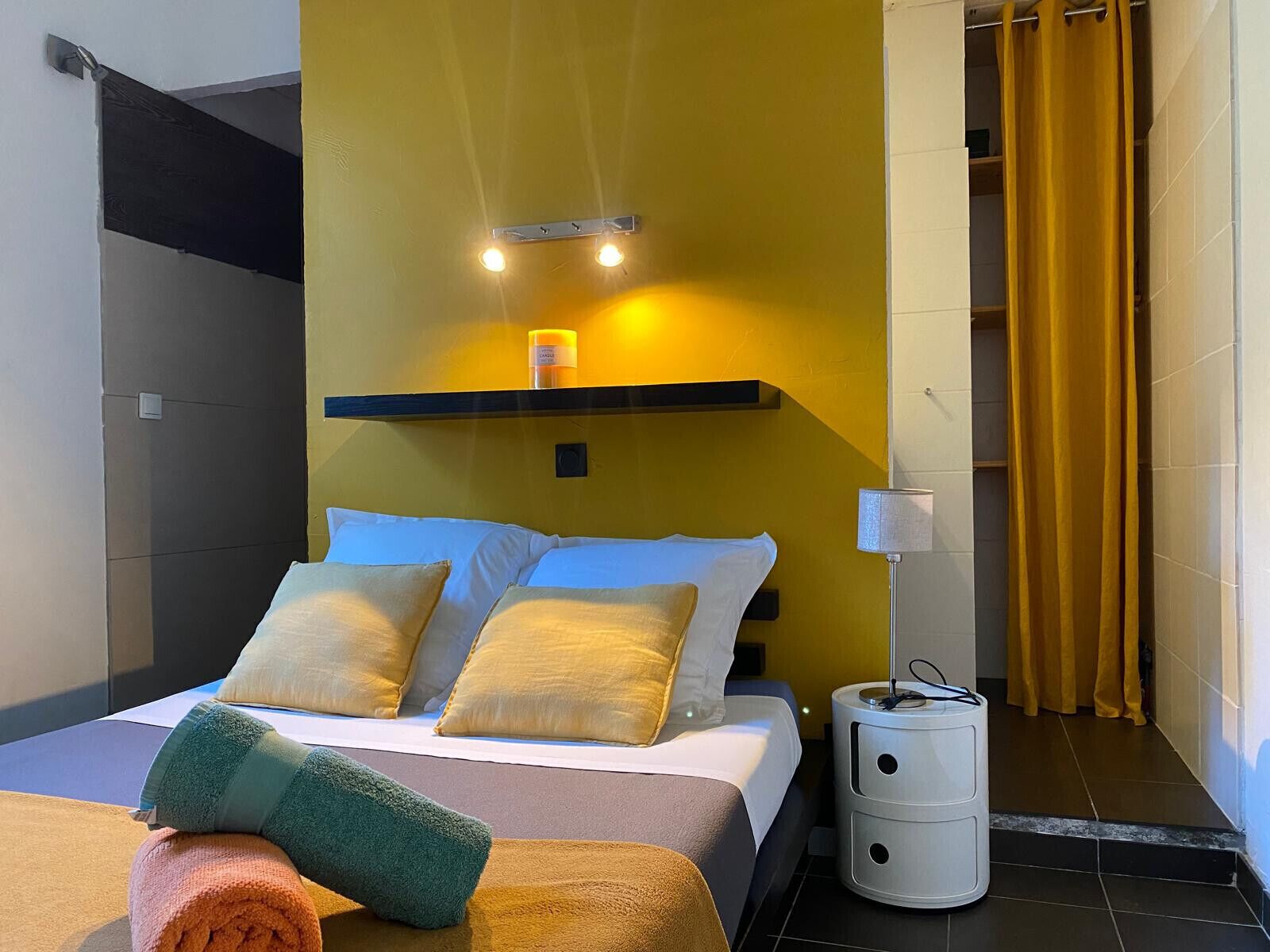 Ein modernes Hotelzimmer mit Bett, Kissen, einem Nachttisch und einem Badezimmer mit gelbem Vorhang.