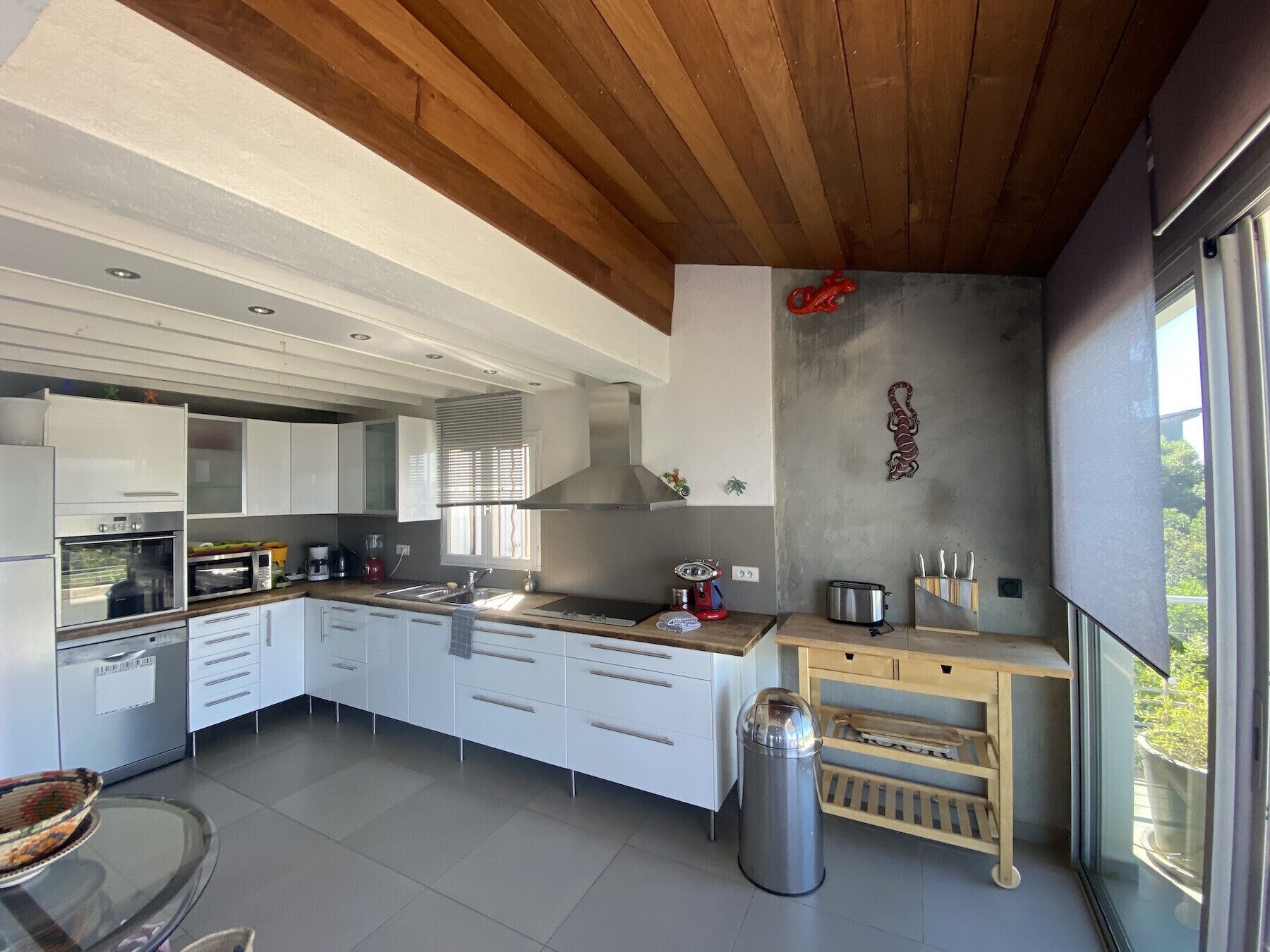 A modern kitchen with white cabinets, a stainless steel range hood, and a large window providing a view of the outdoors.