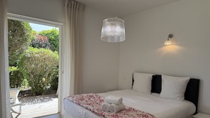 Ein Schlafzimmer mit Bett, Nachttisch, Hängeleuchte und Blick auf einen Garten durch eine Schiebetür.