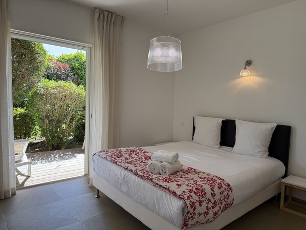 A bedroom with a bed, a bedside table, a hanging light fixture, and a view of a garden through a sliding door.