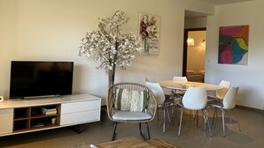 Ein modernes Wohnzimmer mit Flachbildfernseher, einem Esstisch mit Stühlen, einer Zierpflanze und Bildern an der Wand.