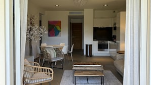 Ein modernes Wohnzimmer mit Essbereich, einer Couch, Korbstühlen, einem Couchtisch und einem Fernseher im Hintergrund.