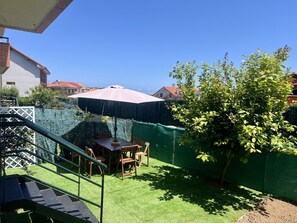 Um quintal com mesa e cadeiras de madeira, gramado verde e uma árvore.