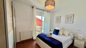 Een slaapkamer met een bed, nachtkastjes, een radiator, een raam met gordijnen en een plafondlamp.