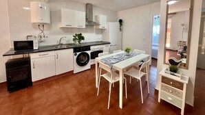 Een praktische keuken met een wasmachine, magnetron, en een eethoek met een tafel en stoelen.