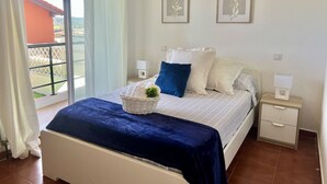 Een slaapkamer met een bed, nachtkastje, lamp en raam met gordijnen.