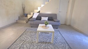 Een woonkamer met een grijze bank, een witte salontafel met een plant en een kamerkleed met een patroon.