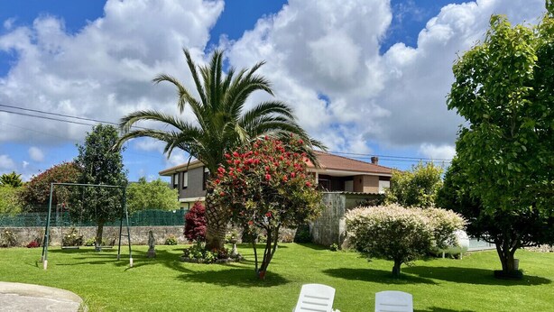 Un giardino curato con due poltrone bianche, una palma e una casa con tetto in tegole.