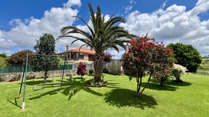 Un giardino curato con altalena, palma e cespugli fioriti.