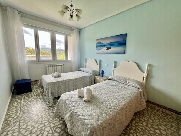 A room with two beds, a window with curtains, a radiator, and a painting on the wall.