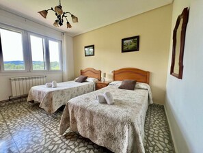 A hotel room with two beds, a radiator, a window with a view, and a chandelier.