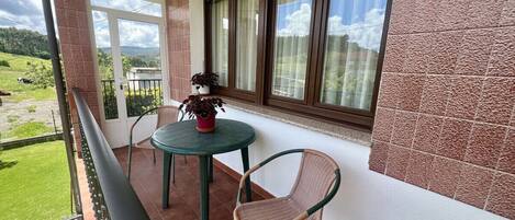 A balcony with a table and chairs, a potted plant, and a view of a green landscape.