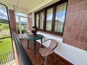 A balcony with a table and chairs, a potted plant, and a view of a green landscape.