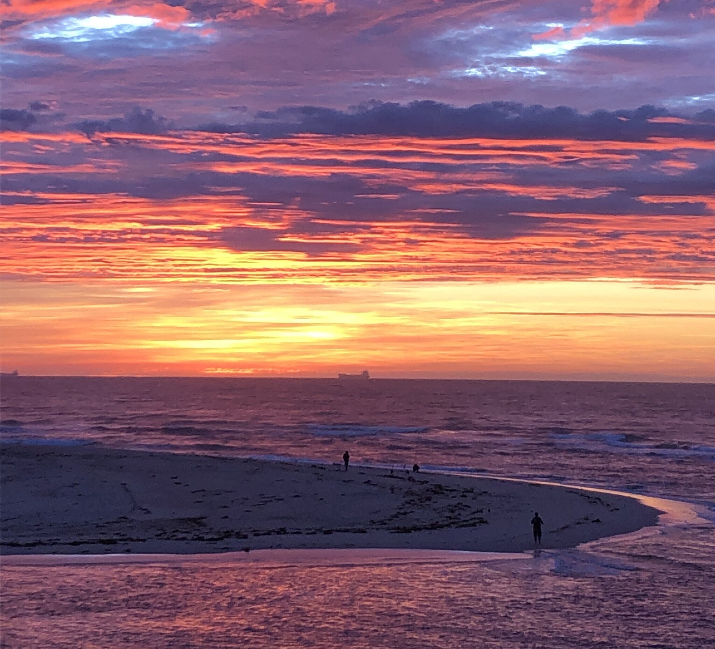Une plage au coucher du soleil, des gens qui se promènent et un bateau au loin.