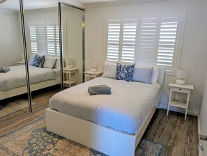 A bedroom with a large mirror, a bed with striped bedding, two bedside tables with lamps, and a patterned rug. - Amazing Ocean Views, Spacious Waterfront Holiday Apartment (The Entrance)