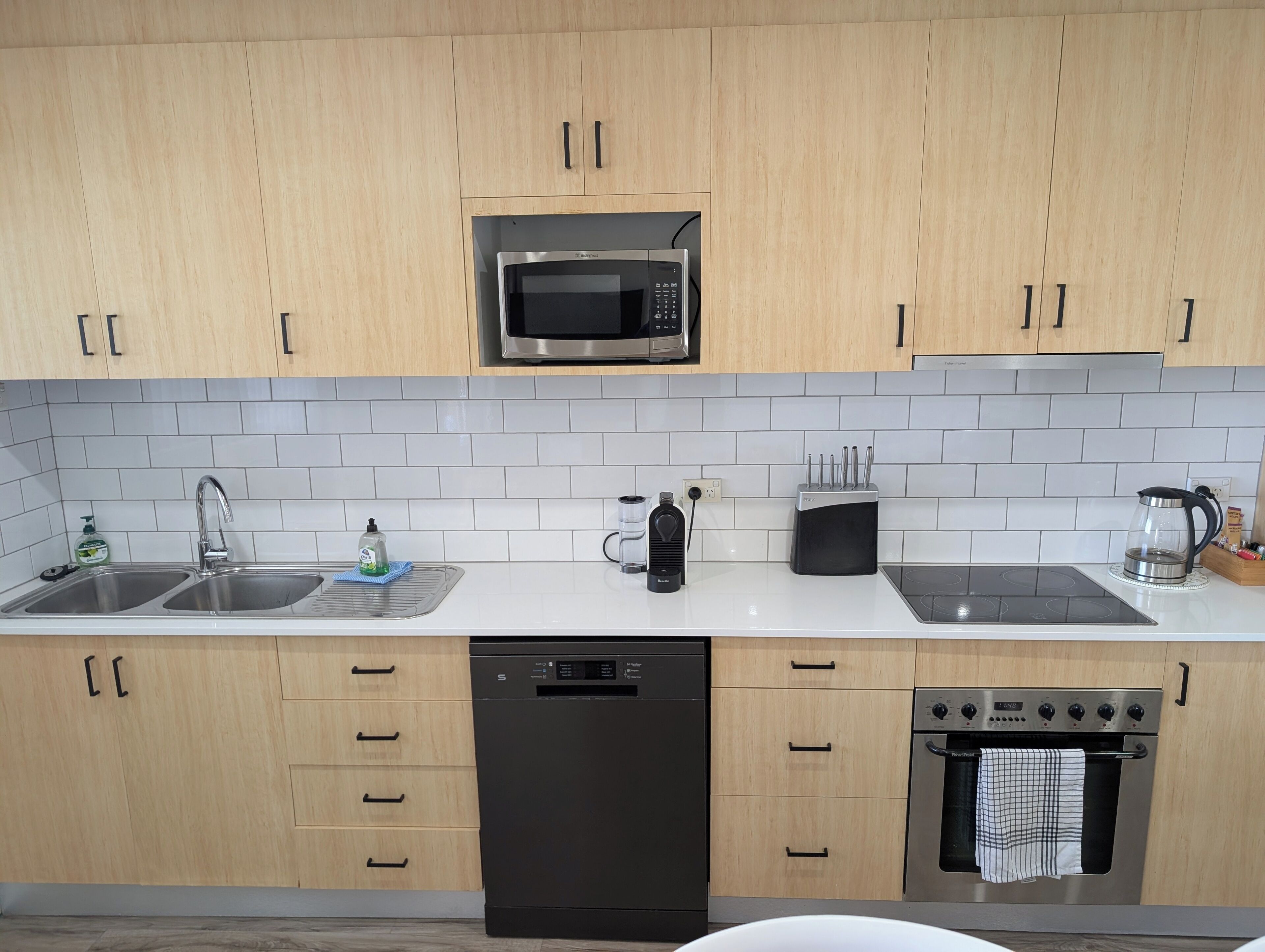 A modern kitchen with wooden cabinets, a stainless steel microwave, a dishwasher, a stove, and a coffee maker.