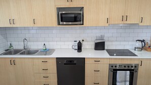 A modern kitchen with wooden cabinets, a stainless steel microwave, a dishwasher, a stove, and a coffee maker. - Amazing Ocean Views, Spacious Waterfront Holiday Apartment (The Entrance)