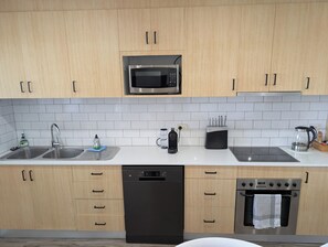 Une cuisine moderne avec des meubles en bois, un four à micro-ondes en acier inoxydable, un lave-vaisselle, une cuisinière et une machine à café.