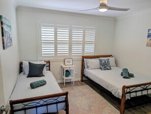 A bedroom with two single beds, a ceiling fan, a window with blinds, and a small bedside table with a vase. - Amazing Ocean Views, Spacious Waterfront Holiday Apartment (The Entrance)