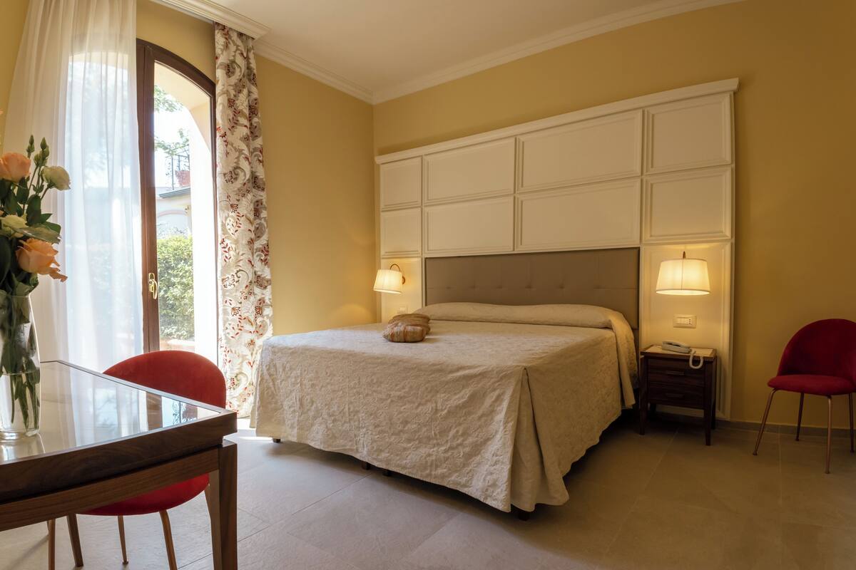 A bedroom with a bed, bedside lamps, a table with chairs, and a vase with flowers.
