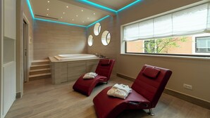 Un moderno cuarto de spa con una bañera grande, dos sillones de masaje rojos y un ventanal con vistas al exterior.