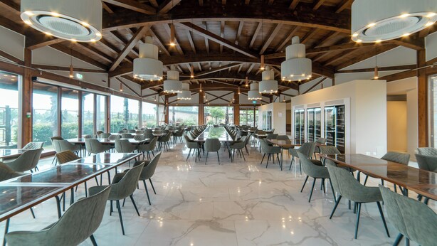 Un comedor amplio con techos altos y ventanas grandes, que presenta mobiliario moderno y abundante luz natural.