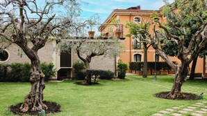 Un patio con árboles maduros, un edificio de ladrillo con ventanas arqueadas y un césped bien cuidado.