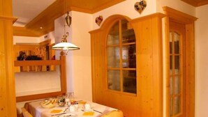 A dining area with a table set for two, wooden cabinets, and a window with frosted glass. - Design Chalet Zirm - Check-in at Olympia Hotel (Livinallongo del Col di Lana)
