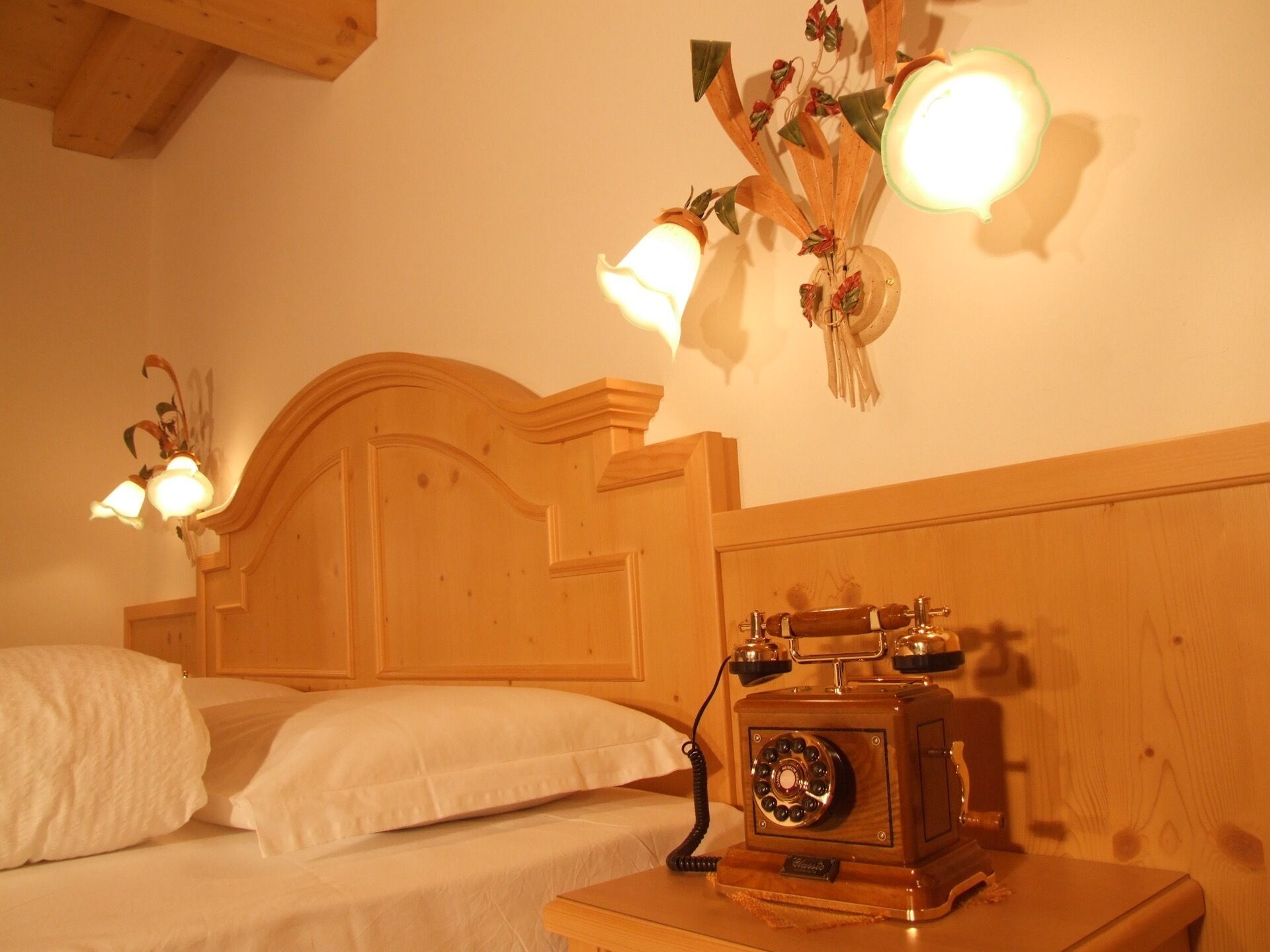 A wooden bed with white linens, a vintage rotary phone, and wall-mounted light fixtures.