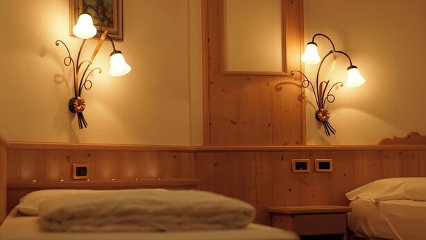 A hotel room with a wooden headboard, two bedside tables, a bed with a white duvet, and wall-mounted sconces with a floral design.