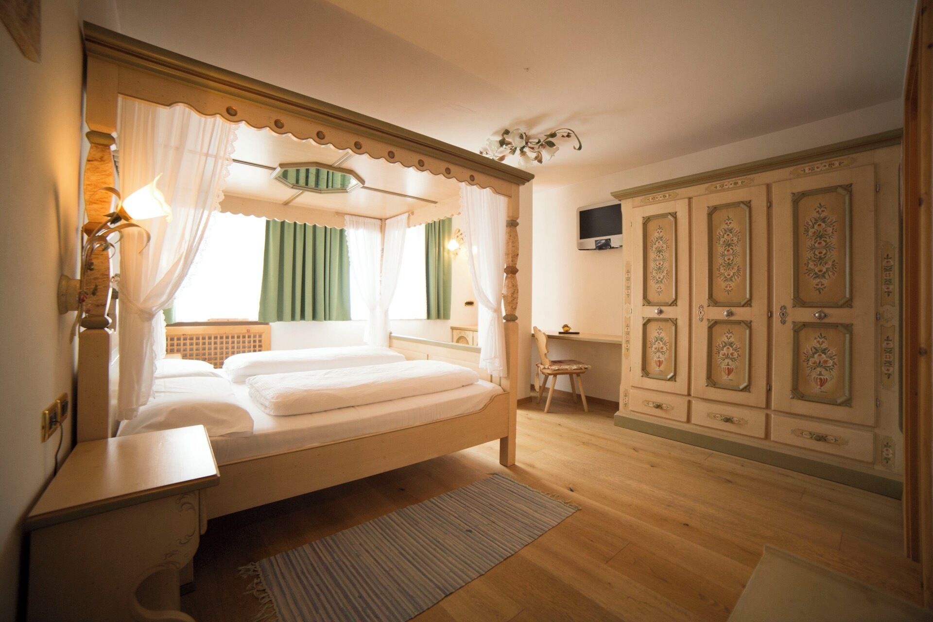 Una camera da letto con un letto a baldacchino, un comodino, una sedia, un armadio e una televisione a parete.