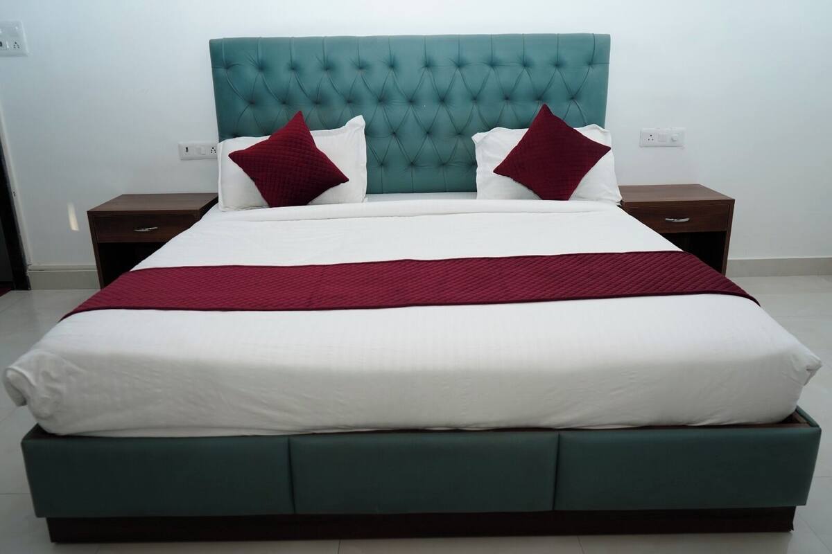 A bed with a teal headboard, white bedding, and two red pillows.