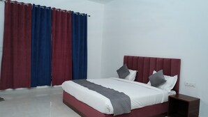 A modern bedroom with a large bed, a nightstand, and a window with red and blue curtains.