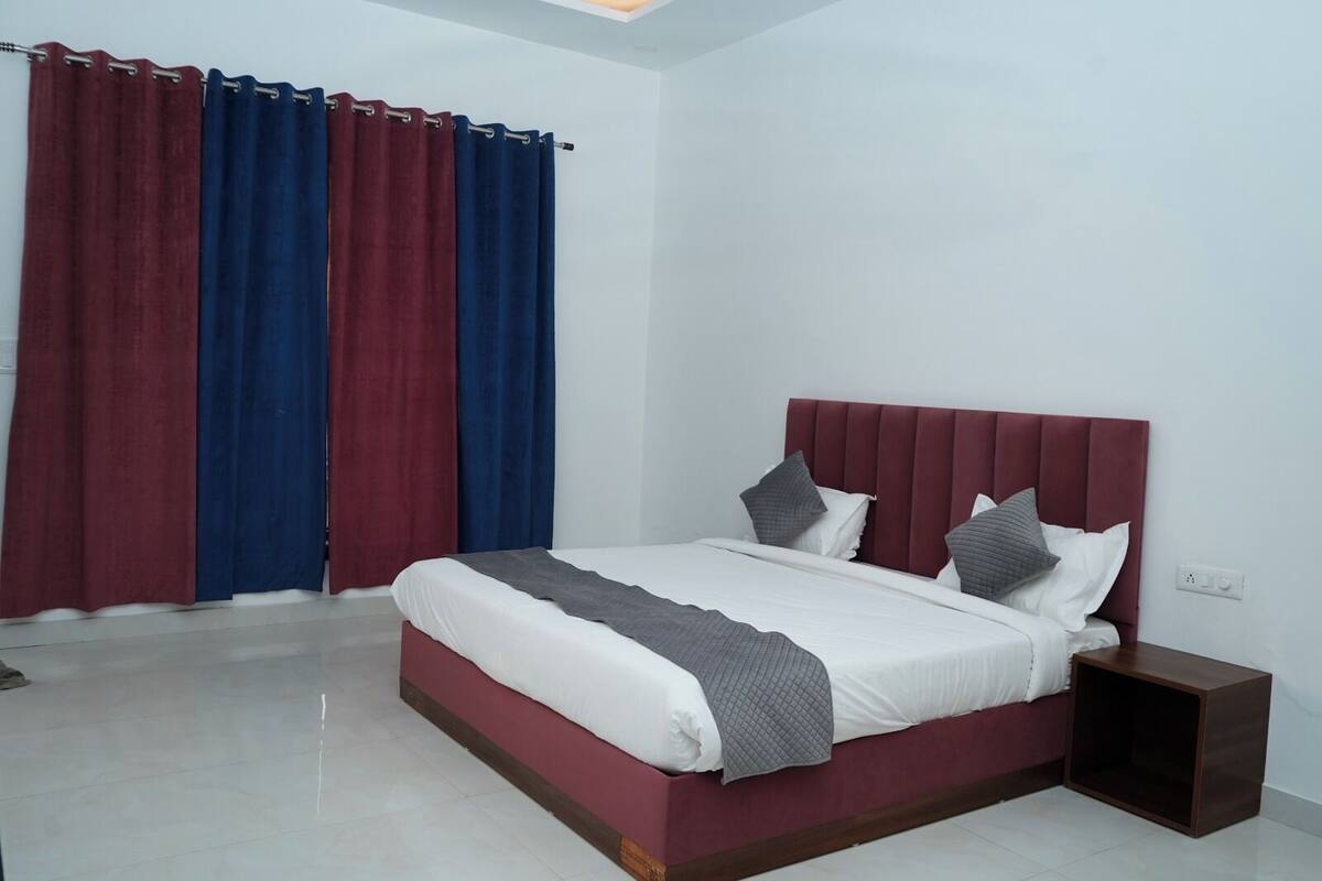 A modern bedroom with a large bed, a nightstand, and a window with red and blue curtains.