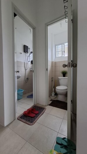 Een smalle gang die leidt naar een badkamer met een toilet, een douche en een klein raam.