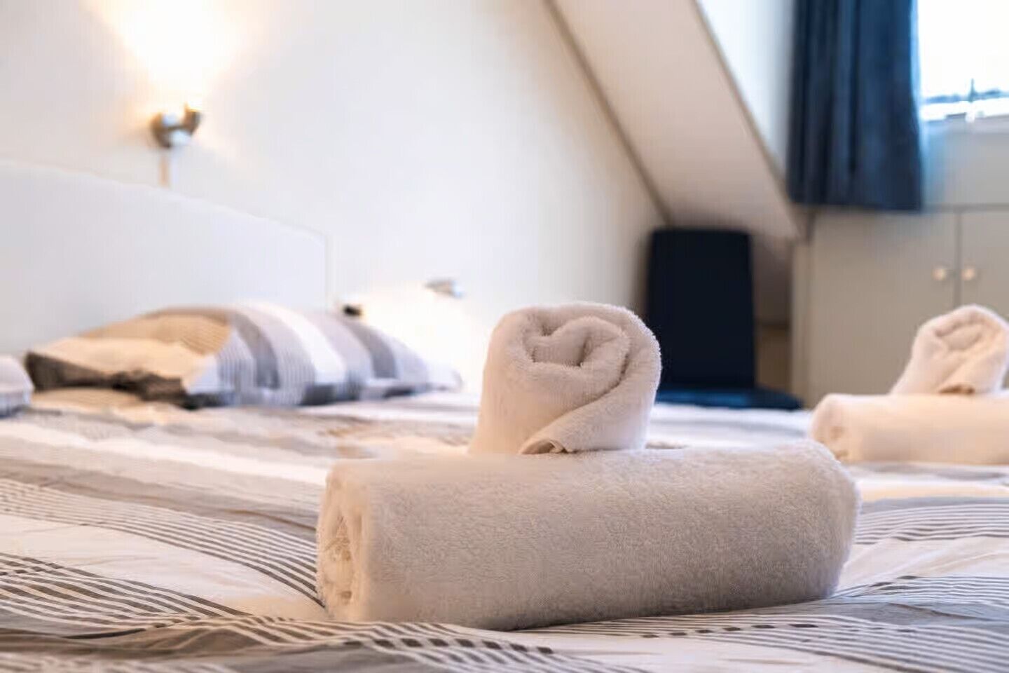 Een hotelkamer met een netjes opgemaakt bed, een kussen en een opgerolde handdoek op het bed.