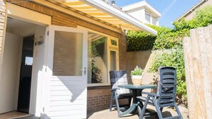 A patio with a table and chairs, a sliding glass door, and a brick wall with greenery. - Duinrust - Cozy-holiday-house-close-to-beach (Egmond aan Zee)