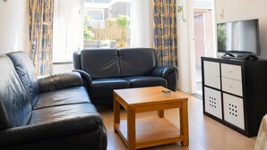 A living room with a black leather sofa, a wooden coffee table, and a TV on a cabinet. - Duinrust - Cozy-holiday-house-close-to-beach (Egmond aan Zee)