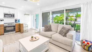 A modern living room with a sofa, a coffee table, and a kitchen area with a microwave and oven. - NEW LISTING! Village Breeze III - Heated Pool, Private Patio, Village and Beach! (Siesta Key)