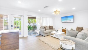 A modern living room with a sofa, coffee table, and a TV mounted on the wall. - NEW LISTING! Village Breeze III - Heated Pool, Private Patio, Village and Beach! (Siesta Key)