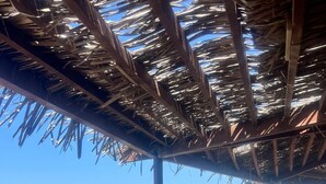 Una terrazza in legno con tetto di paglia che si affaccia su una spiaggia.
