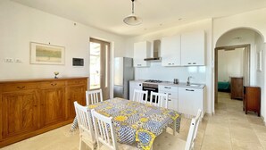 Una cucina compatta con mobili bianchi, un tavolo da pranzo con tovaglia fantasia e un pensile in legno con cassetti.