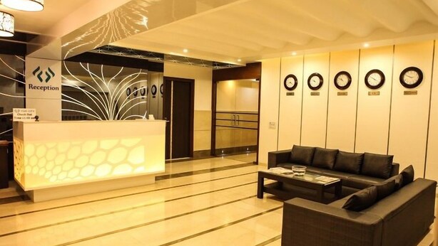 A reception area with a reception desk, a sofa, and a wall with clocks. - Hotel Fun City (Navsari)