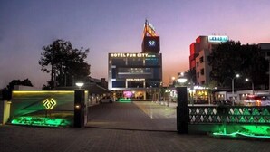 A hotel entrance with a neon sign, a paved walkway, and a gated area. - Hotel Fun City (Navsari)