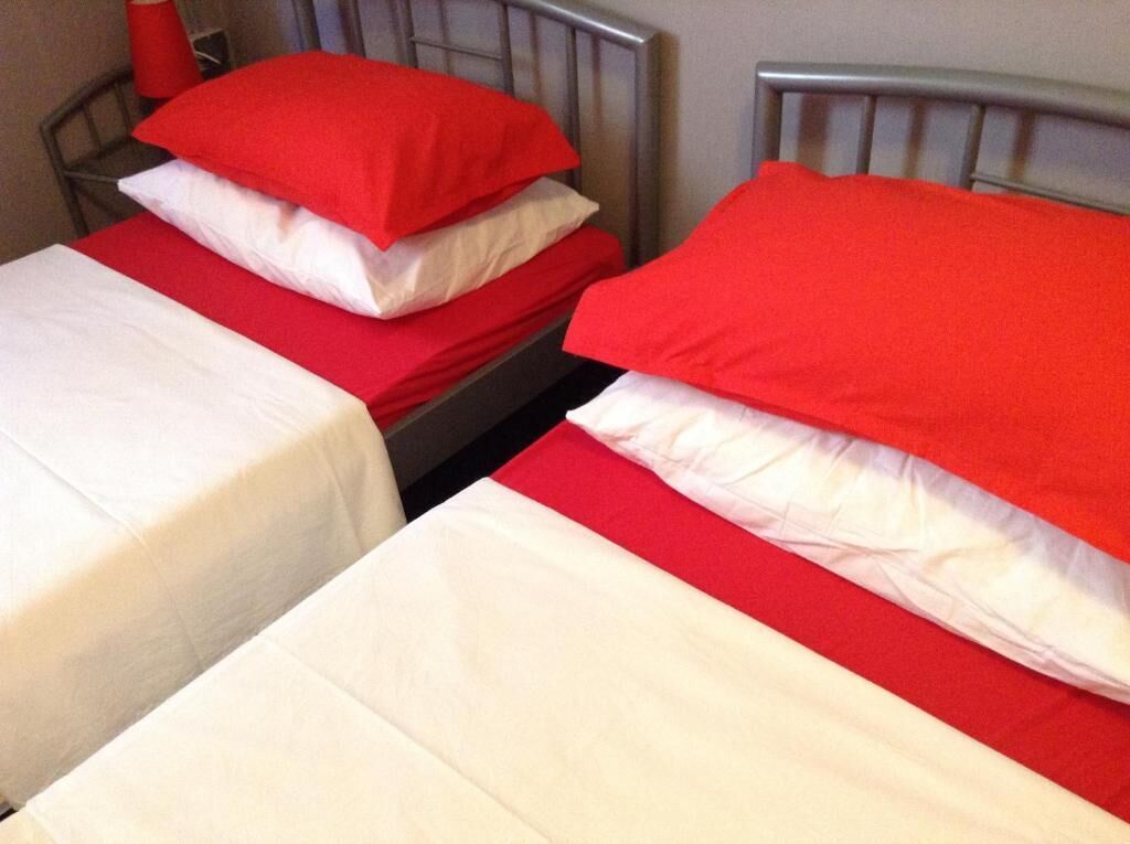 Two single beds with red and white bedding, metal headboards, and a red pillow on one bed.